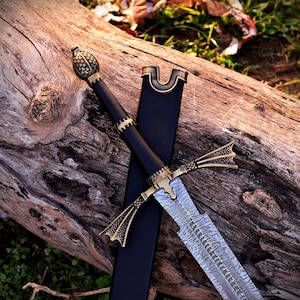 May include: A sword with a patterned Damascus steel blade, a black handle, and an ornate brass-colored pommel and crossguard. The sword is accompanied by a black scabbard, featuring a matching brass-colored throat piece at the top.