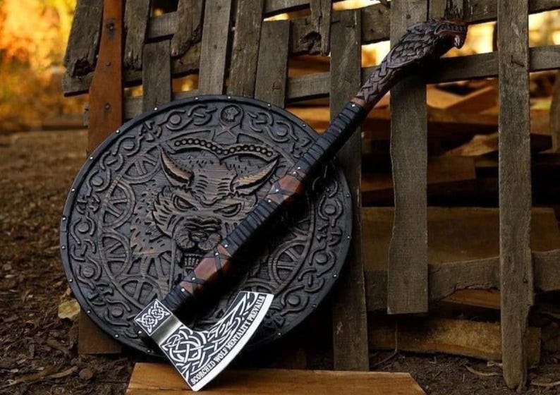 May include: A dark brown wooden axe with a carved wolf head on the handle and a silver blade featuring intricate knotwork and the text "SCORCHED WOLF MENTALITY PREVAILS," resting against a circular wooden shield with a carved wolf face design.