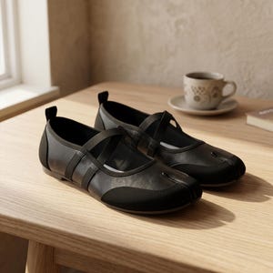 May include: A pair of black split-toe flats featuring a smooth leather-like finish, a rounded toe box with a distinct separation, and a crisscross elastic strap across the top. Each shoe includes a small black pull tab at the heel for easy wear.