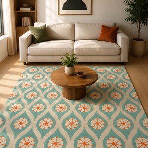 May include: A rectangular area rug featuring a repeating pattern of teal wave-like shapes and orange circular starburst motifs on a cream background. The rug covers the floor in front of a sofa and a round wooden coffee table in a living room.
