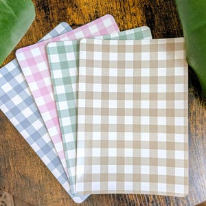 May include: A set of four rectangular placemats featuring a classic gingham check pattern. Each placemat displays a different colour combination of white paired with either light blue, soft pink, sage green, or a neutral tan, all with rounded corners.