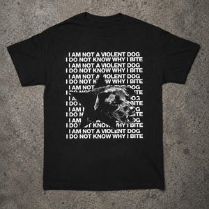 Könnte beinhalten: Ein schwarzes T-Shirt mit kurzen Ärmeln und einer weißen Grafik eines Hundekopfes in einem Stern. Der Hintergrundtext wiederholt die Sätze I AM NOT A VIOLENT DOG und I DO NOT KNOW WHY I BITE in weißen Großbuchstaben auf der Brustpartie.