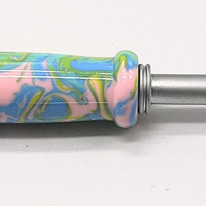 May include: A pink, blue, and green marbled crochet hook with a silver metal hook.