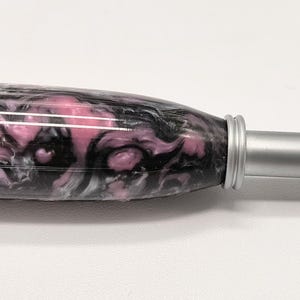May include: A pink and black marbled crochet hook with a silver metal handle. The hook size is 6.5 mm.