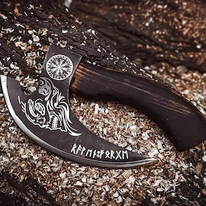 May include: A black metal axe with a curved blade featuring a white engraved wolf head design, a circular Vegvisir symbol, and runic text reading Rᛖᛈᛗᚦᚠᚱᛉᛗ. The axe has a dark, polished wooden handle with a curved shape, showcasing detailed craftsmanship.