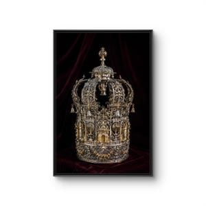 May include: A silver and gold-toned crown featuring intricate filigree metalwork, small hanging bells, and detailed architectural motifs including menorahs and arched doorways. The crown is displayed against a dark, deep red velvet fabric.