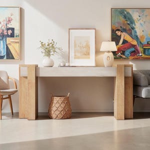 May include: A rectangular console table with a light-toned wooden frame and a central horizontal panel. The table features thick, vertical support legs on each side and a smooth, flat top surface, providing a sturdy structure for display.