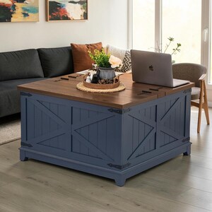 May include: A square coffee table with a dark wood top and a navy blue base featuring a diagonal cross-brace design. The table has black metal hinges at the corners and along the top surface. A laptop and a small woven tray with plants sit on top.