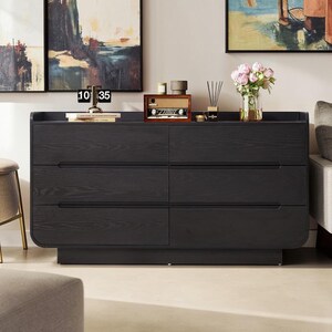 May include: A black wooden dresser featuring six drawers with integrated horizontal handles and rounded corners. The top surface holds a flip clock displaying 10 35, a wooden radio, a small candle, a reed diffuser, and a glass vase with pink flowers.