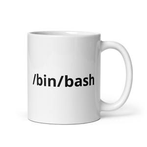 Puede incluir: Una taza de cerámica blanca con el texto negro /bin/bash impreso en el frente. La taza tiene un acabado liso y brillante, un cuerpo cilíndrico y un asa curva en el lado derecho, ofreciendo un diseño sencillo y funcional para las bebidas.