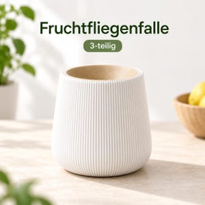Könnte beinhalten: Eine weiße Fruchtfliegenfalle mit gerippter Außenseite und einem hellbraunen, kreisförmigen Einsatz oben. Der Text "Fruchtfliegenfalle" und "3-teilig" ist in dunkelgrüner Schrift über dem Objekt abgebildet und kennzeichnet ein dreiteiliges Set.