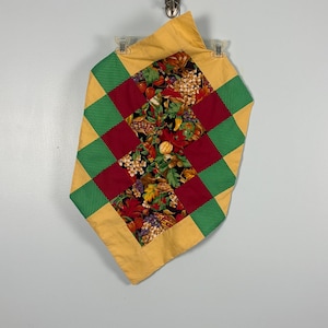 Pode incluir: Um caminho de mesa acolchoado com um painel central de tecido preto com uma estampa colorida de colheita de milho, abóboras e folhas de outono. A borda consiste em quadrados alternados em amarelo mostarda, bordô e verde com bolinhas.