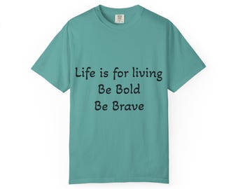 Op de afbeelding: Een blauwgroen t-shirt met korte mouwen en een ronde hals. Op de voorkant staat zwarte tekst met de woorden: Life is for living, Be Bold, Be Brave. Het kledingstuk heeft een standaard pasvorm met een rechte zoom en een label in de nek.
