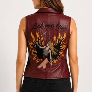 May include: A sleeveless burgundy vest with a collar, featuring an embroidered graphic on the back of a warrior figure holding a spear amidst stylized yellow and black flames, with the text Let me live embroidered in black above the graphic.