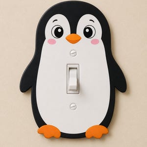 May include: A light switch cover shaped like a penguin with a black and white body, an orange beak, and orange feet. The cover features a central white toggle switch and two silver screws positioned above and below the switch mechanism.