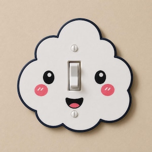 May include: A white cloud-shaped light switch cover with a dark blue border. The cover features a printed face with two black circular eyes, two pink circular cheeks, and a black smiling mouth. A white toggle switch is centered on the plate.