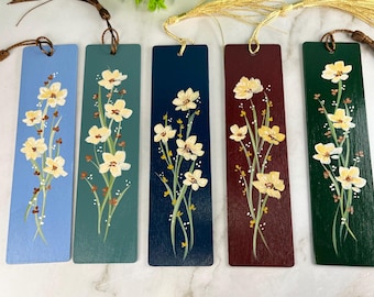 May include: Five rectangular bookmarks in light blue, teal, dark blue, burgundy, and dark green, each featuring a hand-painted design of pale yellow flowers with green stems and leaves, finished with a decorative tassel attached to the top.