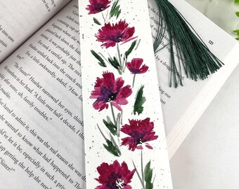 May include: A rectangular paper bookmark featuring a watercolor painting of magenta flowers with green stems and leaves on a white background. The bookmark has a silver metal eyelet at the top with a dark green thread tassel attached to it.