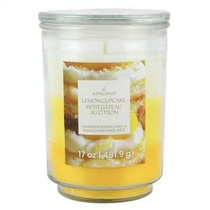 May include: A clear glass jar candle filled with bright yellow wax. The label features a picture of a lemon cupcake with white frosting and the text Ashland Lemon Cupcake Petit Gâteau Au Citron Summer Scented Candle 17 oz | 481.9 g.