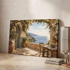 Könnte beinhalten: Ein rechteckiger Leinwanddruck, der eine mediterrane Steinterrasse mit einem Holztisch und einem Stuhl zeigt, mit Blick auf das Meer, eingerahmt von einem steinernen Torbogen, der mit weißen Blütenranken bewachsen ist.