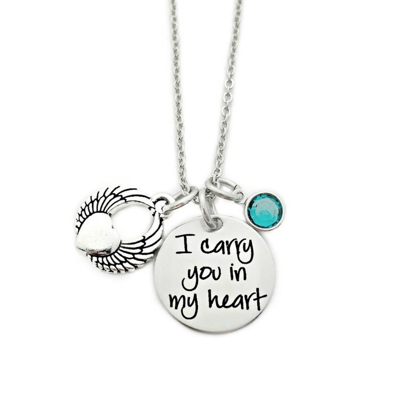 May include: Silver necklace with a heart and wings charm, a small turquoise blue crystal charm, and a round pendant with the inscription "I carry you in my heart".