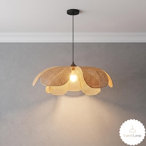May include: A pendant light fixture featuring a woven, tan-colored shade shaped like a multi-layered flower. The shade is suspended by a thin black cord from a black ceiling mount. A single light bulb is visible in the center, emitting a warm glow.