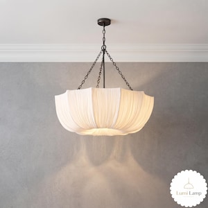 May include: A white fabric pendant light fixture with a pleated, bowl-shaped shade. The lamp is suspended by a dark metal rod and three thin chains connected to a circular ceiling canopy. The fabric emits a soft, diffused glow from within.