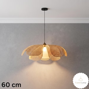 May include: A 60 cm pendant light featuring a woven tan rattan shade shaped like a blooming flower with multiple overlapping petals. The fixture hangs from a thin black cord attached to a black ceiling canopy and emits a warm light.