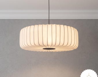 May include: A white, circular, pleated pendant lamp with a thin black cord and a small black circular center accent. The lamp emits a soft, diffused light, creating a rounded, ribbed appearance that hangs from a single vertical wire.