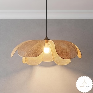May include: A pendant light fixture featuring a woven tan shade shaped like a large flower with multiple overlapping petals. A single light bulb is visible in the center, emitting a warm glow. The text Lumi Lamp is visible in the bottom corner.