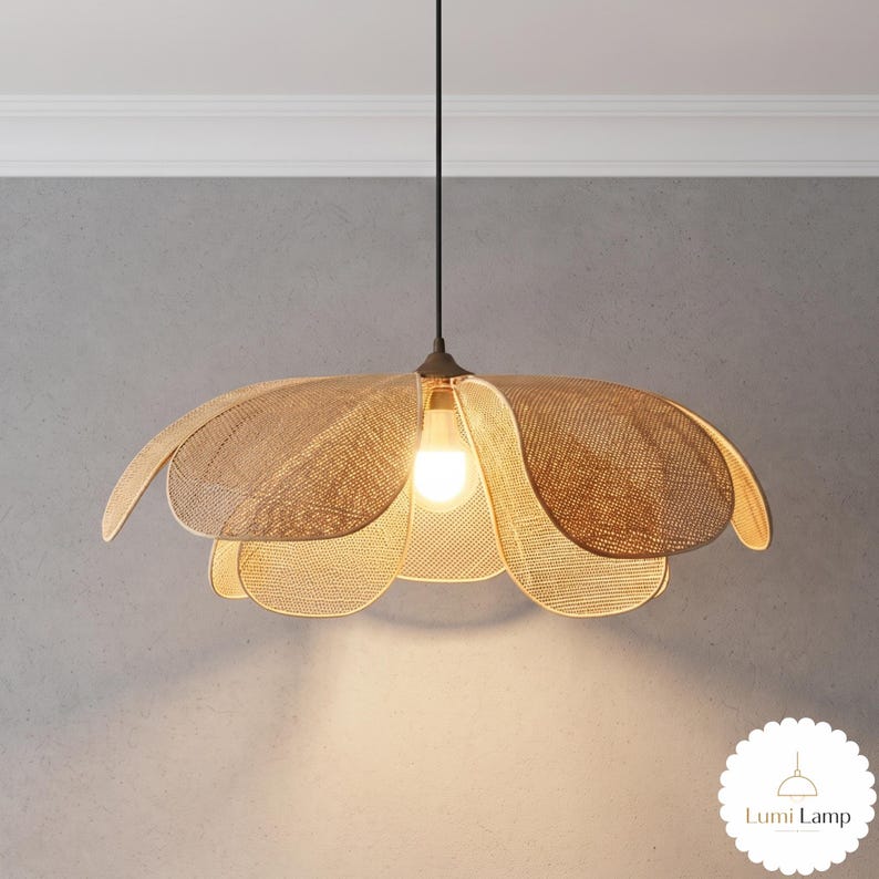 May include: A pendant light fixture featuring a woven tan shade shaped like a large flower with multiple overlapping petals. A single light bulb is visible in the center, emitting a warm glow. The text Lumi Lamp is visible in the bottom corner.