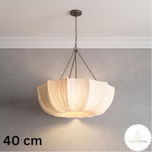May include: A 40 cm pendant light featuring a cream-colored, pleated fabric shade suspended by a dark metal chain and canopy. The fixture has a wide, bowl-like shape with soft folds, emitting a warm glow from the center of the fabric structure.