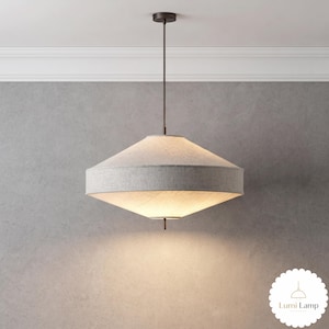 May include: A pendant light fitting featuring a wide, double-conical fabric shade in a light grey textured material. The lamp is suspended by a thin, dark brown metal rod from a matching circular ceiling canopy and includes a small metal finial.