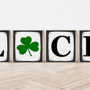Op de afbeelding: Vier zwarte ingelijste borden met een witte achtergrond die "LUCK" spellen met een groene klaver tussen de "L" en de "C".