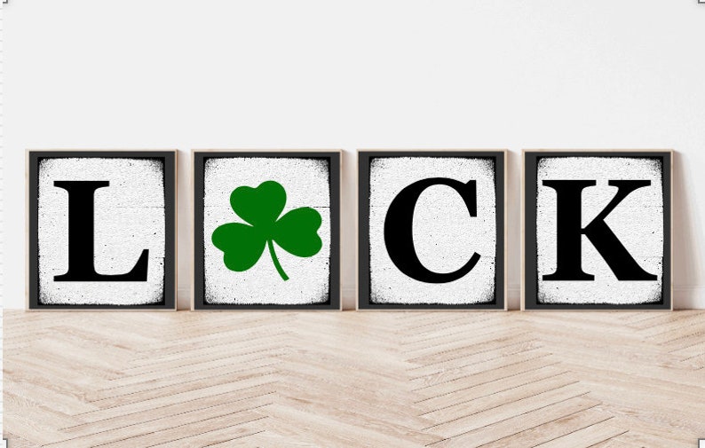 Op de afbeelding: Vier zwarte ingelijste borden met een witte achtergrond die "LUCK" spellen met een groene klaver tussen de "L" en de "C".