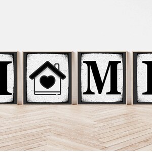 Op de afbeelding: Vier zwarte en witte houten borden die het woord "HOME" spellen met een huissymbool met een hart in het midden van het tweede bord.