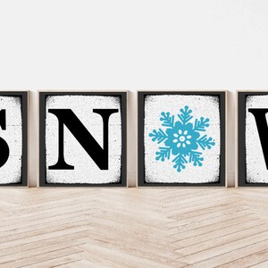 Op de afbeelding: Vier zwarte ingelijste borden met een witte achtergrond. De borden spellen "SNOW" met een blauwe sneeuwvlok in plaats van de "O".