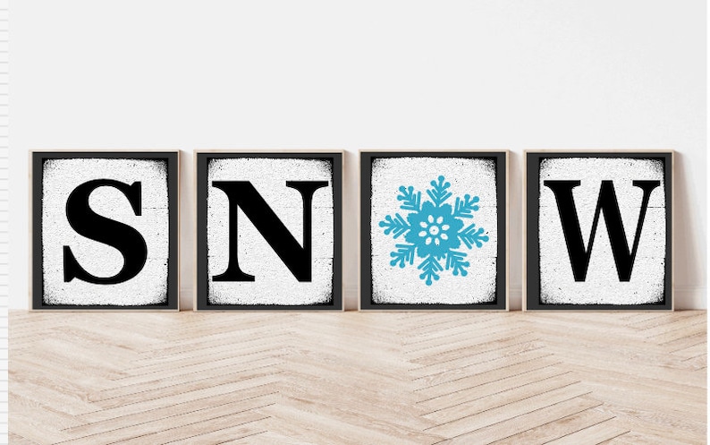Op de afbeelding: Vier zwarte ingelijste borden met een witte achtergrond. De borden spellen "SNOW" met een blauwe sneeuwvlok in plaats van de "O".
