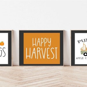 Może przedstawiać: Trzy oprawione wydruki z jesiennymi napisami i ilustracjami. Pierwszy wydruk ma czarną ramkę i napis "Autumn Blessings" z dwoma pomarańczowymi dyniami. Drugi wydruk ma czarną ramkę i napis "Happy Harvest" białym tekstem na ż&oacute;łtym tle. Trzeci wydruk ma czarną ramkę i napis "Pumpkins, Apple Cider & Hay Rides" z zielonym ciężarowym samochodem przewożącym dynie.