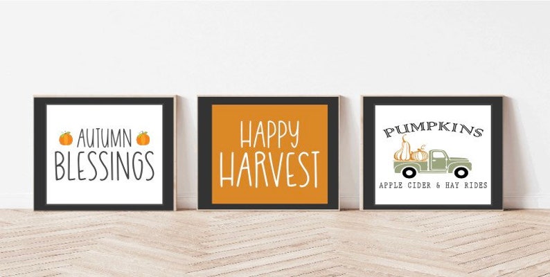 Może przedstawiać: Trzy oprawione wydruki z jesiennymi napisami i ilustracjami. Pierwszy wydruk ma czarną ramkę i napis "Autumn Blessings" z dwoma pomarańczowymi dyniami. Drugi wydruk ma czarną ramkę i napis "Happy Harvest" białym tekstem na ż&oacute;łtym tle. Trzeci wydruk ma czarną ramkę i napis "Pumpkins, Apple Cider & Hay Rides" z zielonym ciężarowym samochodem przewożącym dynie.