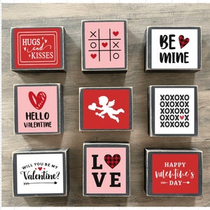K&ouml;nnte beinhalten: Neun Holzbl&ouml;cke mit Valentinstag-Motiven. Die Bl&ouml;cke zeigen S&auml;tze wie "Hugs and Kisses", "Hello Valentine", "Will You Be My Valentine?", "Love", "Be Mine", "XOXOXO" und "Happy Valentine's Day".