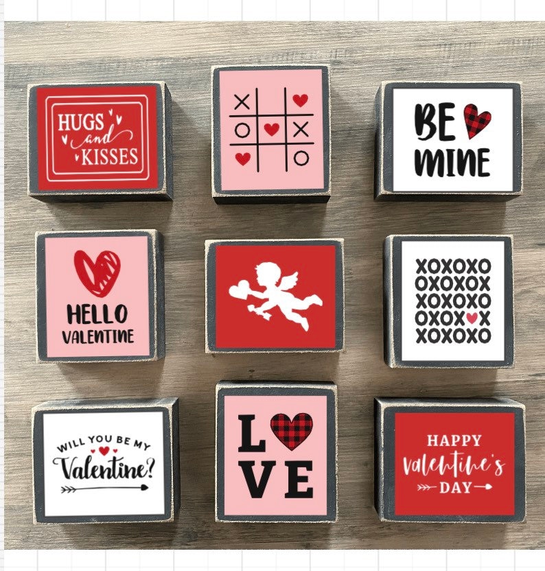K&ouml;nnte beinhalten: Neun Holzbl&ouml;cke mit Valentinstag-Motiven. Die Bl&ouml;cke zeigen S&auml;tze wie "Hugs and Kisses", "Hello Valentine", "Will You Be My Valentine?", "Love", "Be Mine", "XOXOXO" und "Happy Valentine's Day".