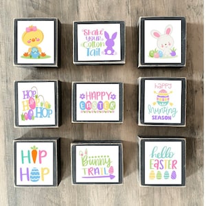 May include: Nine wooden blocks with Easter-themed designs. The blocks feature phrases like "Shake Your Cotton Tail", "Happy Easter", "Bunny Trail", and "Hello Easter". Some blocks also have images of bunnies, chicks, and eggs.