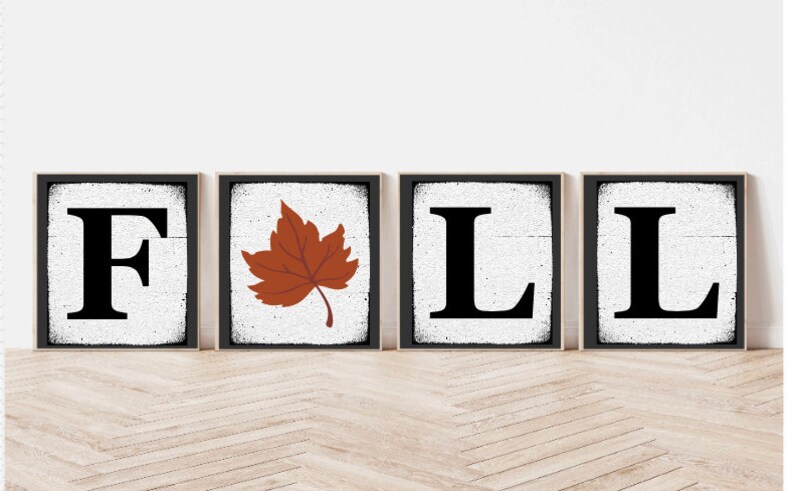 Op de afbeelding: Vier houten borden die het woord "FALL" spellen met een bruin esdoornblad in het midden. De borden hebben een witte achtergrond met zwarte letters en een verweerde look.