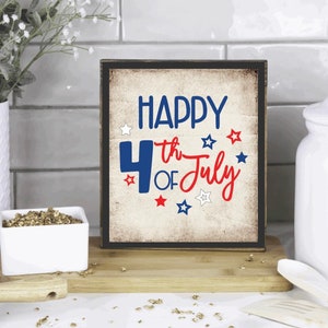 以下が含まれることがあります： 「HAPPY 4th OF July」の文字が青と赤で書かれた、額縁付きの木製サイン。星のアクセントが付いた、使い古されたヴィンテージ風のデザインです。7月4日の装飾品です。