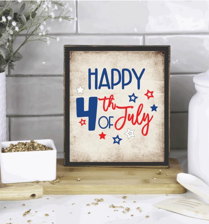 以下が含まれることがあります： 「HAPPY 4th OF July」の文字が青と赤で書かれた、額縁付きの木製サイン。星のアクセントが付いた、使い古されたヴィンテージ風のデザインです。7月4日の装飾品です。