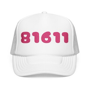 May include: A white trucker cap with a mesh back and a solid front panel. The front features the number 81611 in a bold, textured pink font. Small heart-shaped cutouts are integrated into the digits 8, 1, and 6 of the pink graphic design.
