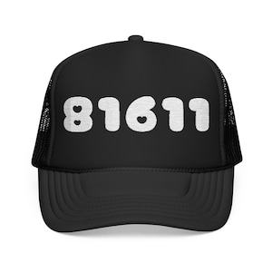 May include: A black trucker cap featuring a white embroidered design of the number 81611 on the front panel. The numbers are stylised with small heart cutouts integrated into the digits. The cap has a structured front and a mesh back panel.