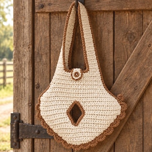 May include: A cream-colored crochet handbag with a brown border and handle. The bag features a diamond-shaped cutout in the center, a scalloped bottom edge, and a small circular button closure at the top of the main body, all crafted in yarn.