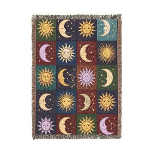 May include: A rectangular woven throw blanket featuring a grid pattern of celestial motifs including suns, crescent moons, and stars. The design uses a palette of deep blue, dark green, maroon, yellow, and purple, finished with a fringed edge.